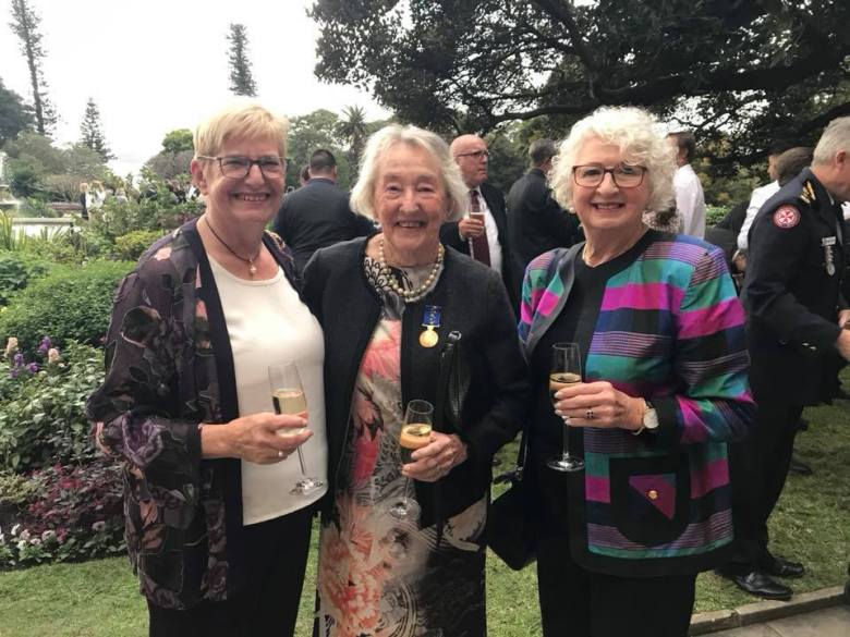 Picture of three well dressed women with glasses of champagne celebrating in the garden of Government House