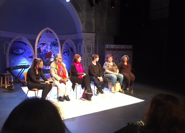 Picture of a stage with six people sitting on chairs having a discussion