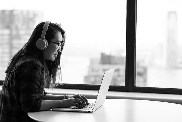 Picture of a woman using a computer and listening to headphones
