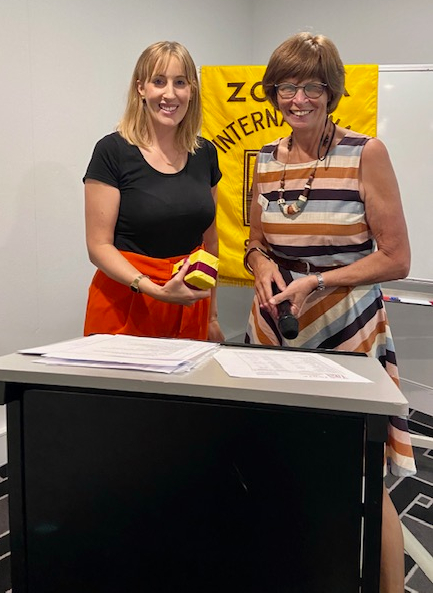 Two women smiling at camera, one presenting the other with a gift